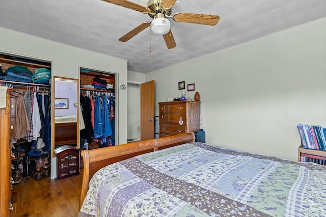 bedroom with a textured ceiling, ceiling fan, wood finished floors, and two closets