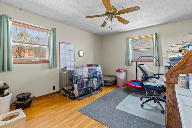 home office with a textured ceiling, wood finished floors, a ceiling fan, and baseboards