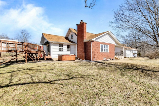 rear view of property featuring brick siding, a yard, a wooden deck, a chimney, and a hot tub