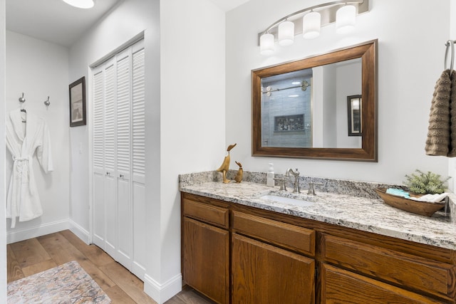 bathroom with tiled shower, wood finished floors, vanity, and baseboards