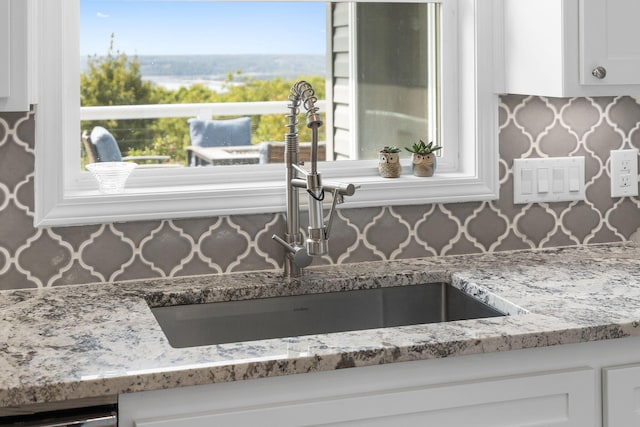 kitchen featuring dishwashing machine, a sink, white cabinetry, decorative backsplash, and light stone countertops