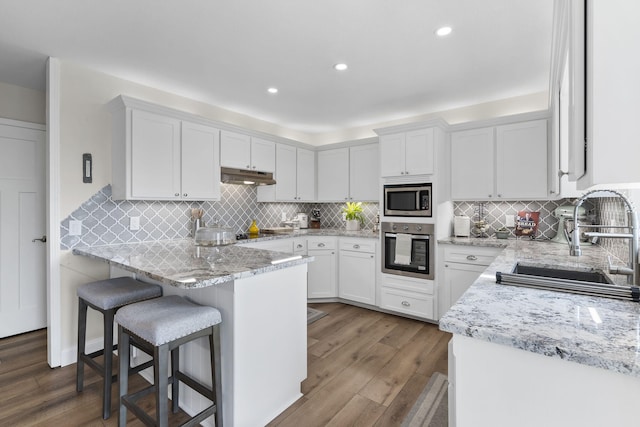 kitchen featuring stainless steel appliances, white cabinetry, a sink, and under cabinet range hood