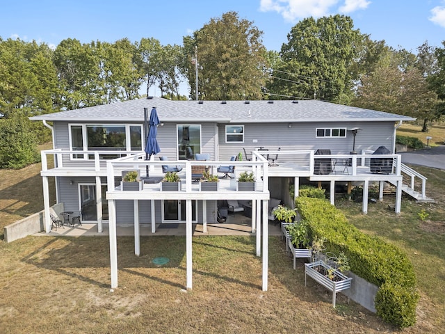 rear view of house with a garden, roof with shingles, a lawn, and a patio