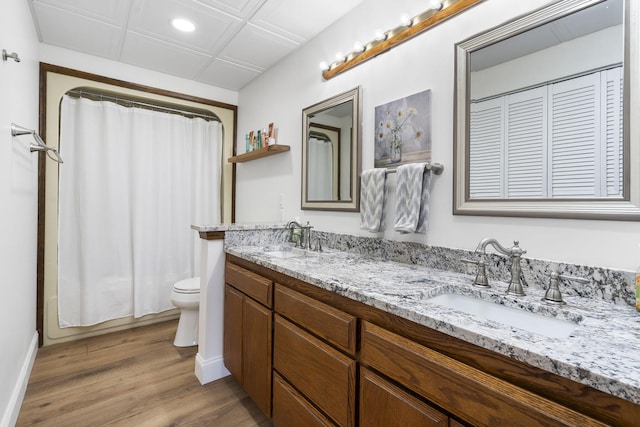 bathroom with toilet, double vanity, a sink, and wood finished floors