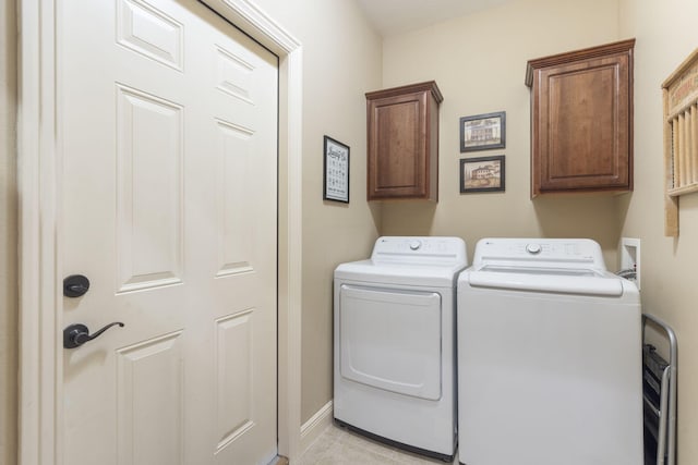 clothes washing area featuring light tile patterned floors, cabinet space, baseboards, and separate washer and dryer