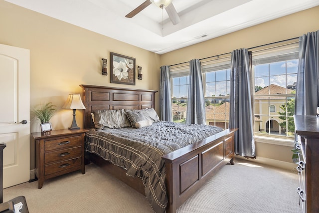 bedroom featuring multiple windows, a raised ceiling, and light colored carpet