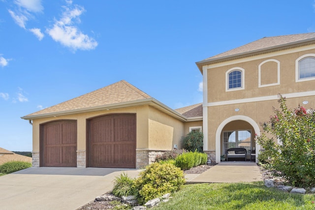 view of front facade with a garage, a shingled roof, concrete driveway, stone siding, and stucco siding