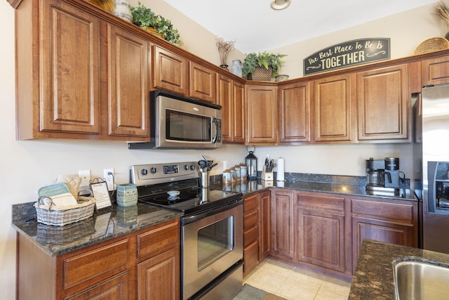 kitchen with appliances with stainless steel finishes, brown cabinets, dark stone countertops, and light tile patterned floors