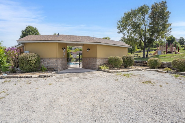 view of front of home featuring stone siding, a gate, a playground, and stucco siding