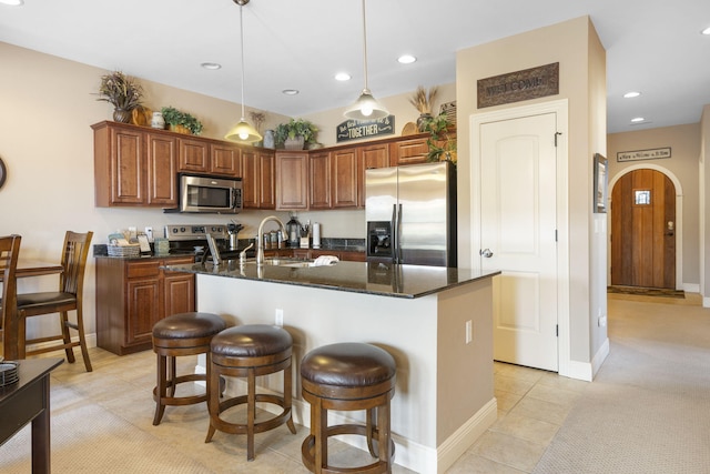 kitchen with arched walkways, appliances with stainless steel finishes, a kitchen island with sink, pendant lighting, and a sink