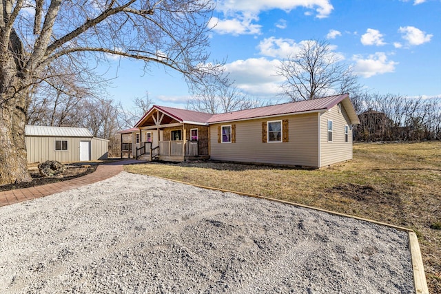 ranch-style home featuring driveway, metal roof, an outbuilding, covered porch, and a front lawn