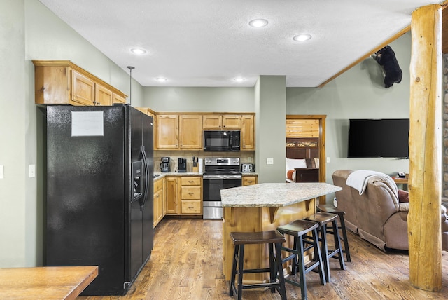 kitchen with light wood-style flooring, a kitchen breakfast bar, a center island, light countertops, and black appliances