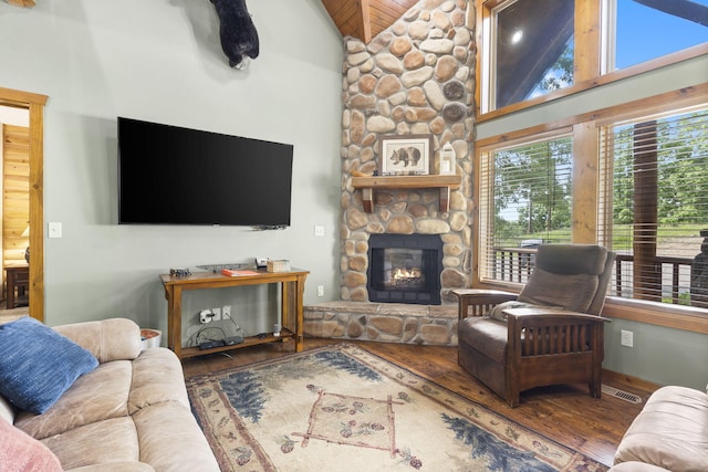 living area featuring high vaulted ceiling, visible vents, wood finished floors, and a stone fireplace