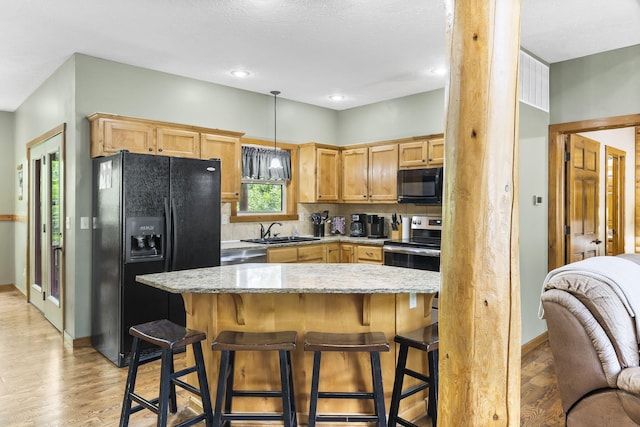 kitchen featuring light stone counters, a breakfast bar area, light wood finished floors, a sink, and black appliances