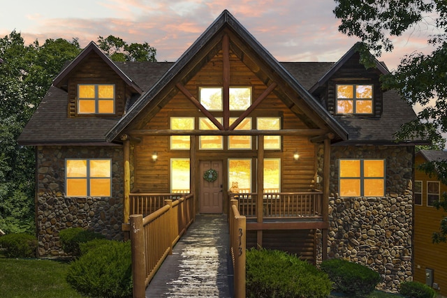 log-style house featuring covered porch, stone siding, and roof with shingles