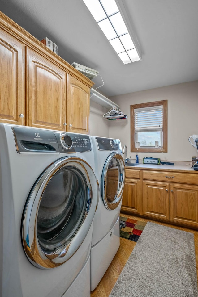 laundry area featuring cabinet space, washer and clothes dryer, a sink, and light wood finished floors