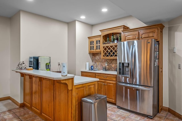 kitchen with a peninsula, light countertops, backsplash, stainless steel fridge, and glass insert cabinets