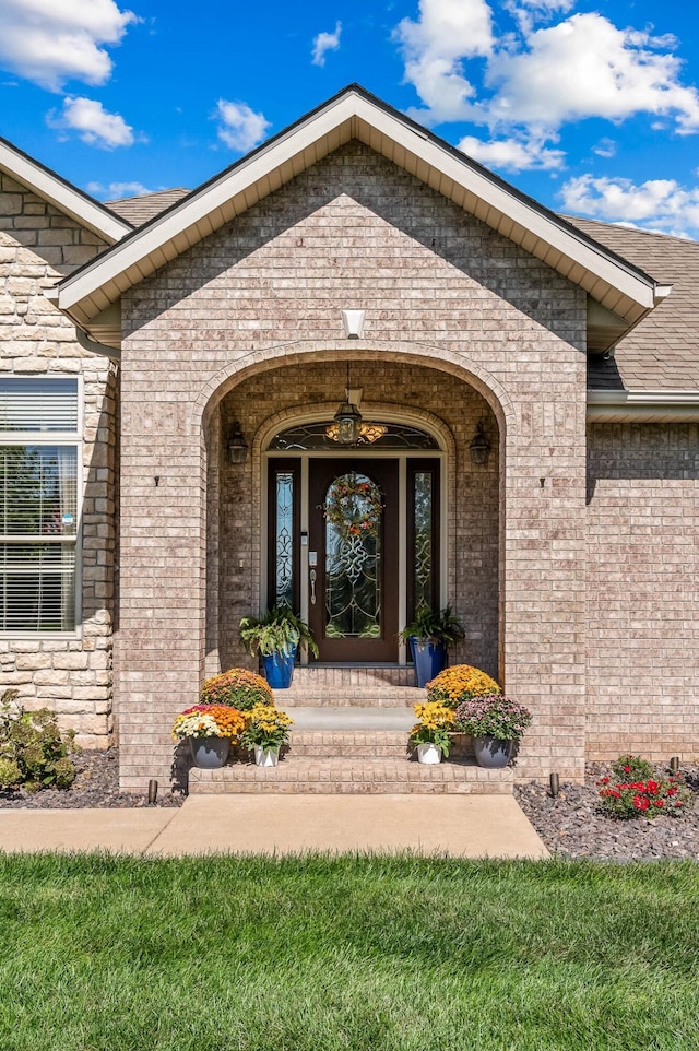 doorway to property with a shingled roof and brick siding