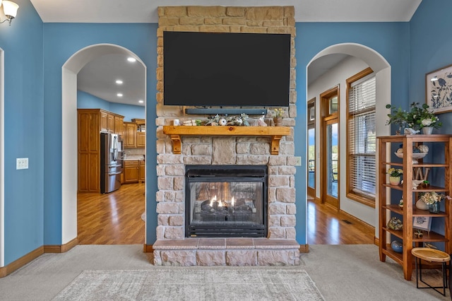 living area with arched walkways, a stone fireplace, baseboards, and light wood finished floors