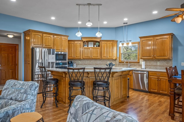 kitchen featuring appliances with stainless steel finishes, light wood-type flooring, a center island, and light countertops