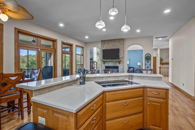 kitchen featuring visible vents, open floor plan, black electric stovetop, light countertops, and a stone fireplace