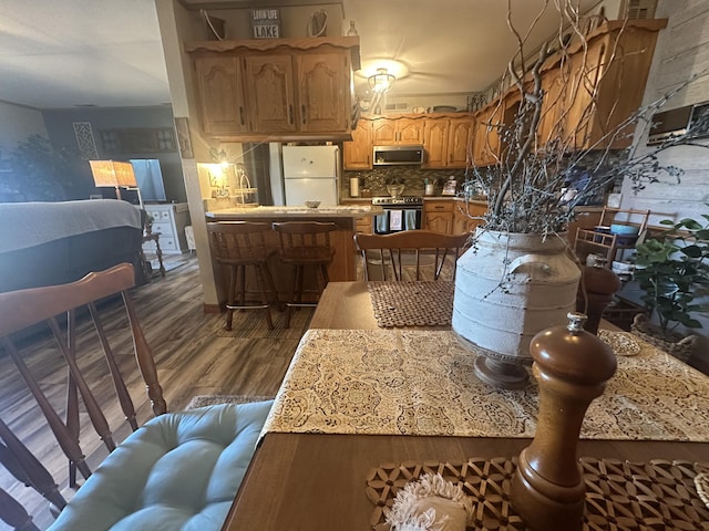 kitchen featuring tasteful backsplash, a peninsula, dark wood-style floors, brown cabinetry, and stainless steel appliances