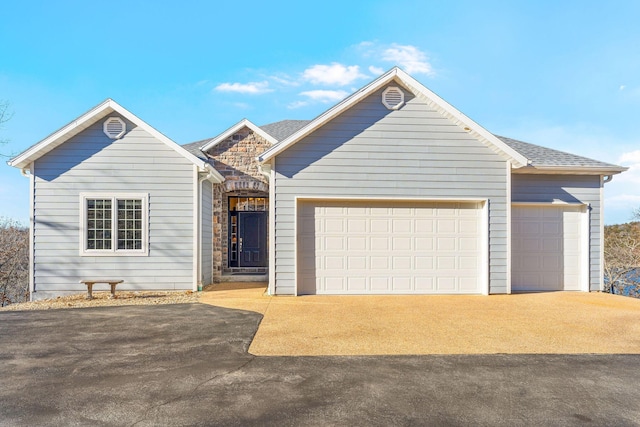 ranch-style home with a garage, driveway, a shingled roof, and stone siding