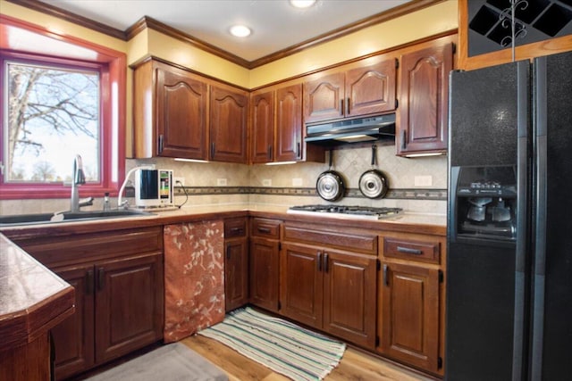 kitchen featuring a sink, decorative backsplash, stainless steel gas stovetop, under cabinet range hood, and black refrigerator with ice dispenser