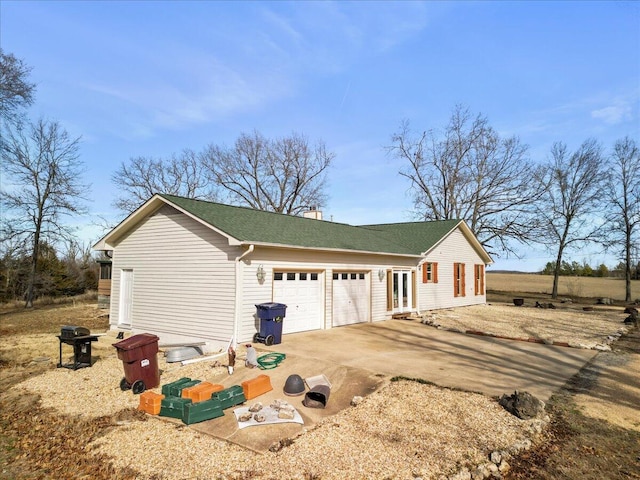 view of side of property featuring driveway, a chimney, a garage, and a shingled roof