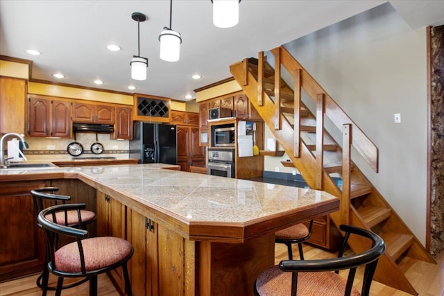 kitchen featuring tile countertops, light wood finished floors, a sink, stainless steel appliances, and a kitchen breakfast bar