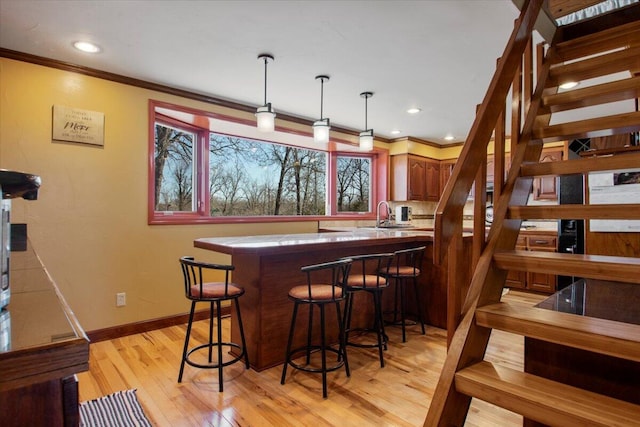 bar with pendant lighting, crown molding, light wood finished floors, baseboards, and stairs