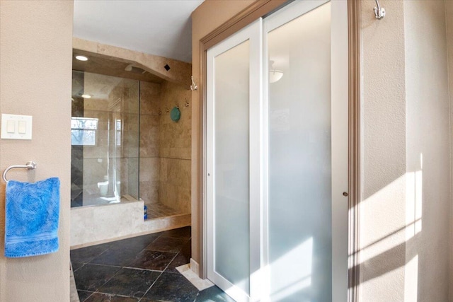 full bath featuring stone tile floors and a shower stall