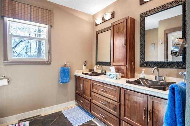 bathroom with double vanity, baseboards, visible vents, and a sink