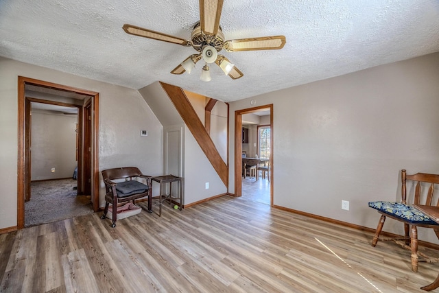 living area featuring a textured ceiling, ceiling fan, light wood-type flooring, and baseboards