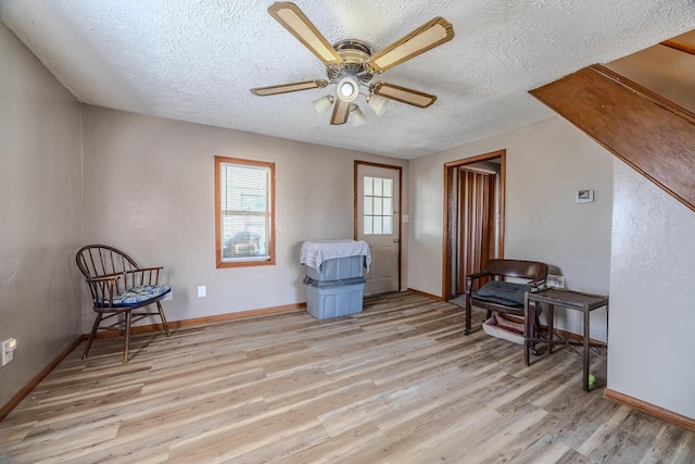 sitting room featuring a textured ceiling, ceiling fan, light wood-style flooring, and baseboards