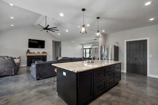 kitchen with concrete flooring, dark cabinets, stainless steel fridge with ice dispenser, a center island, and a glass covered fireplace