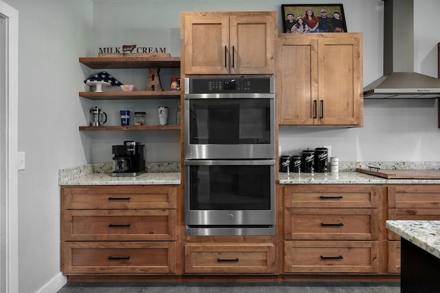 kitchen featuring double oven, wall chimney range hood, light stone countertops, stovetop, and baseboards