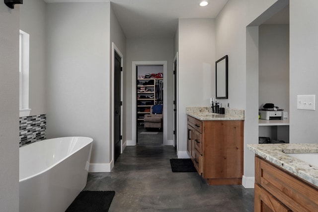 full bathroom featuring concrete floors, vanity, baseboards, a freestanding bath, and a walk in closet