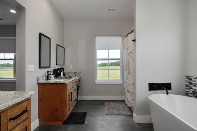 bathroom with vanity, baseboards, a freestanding bath, visible vents, and finished concrete floors