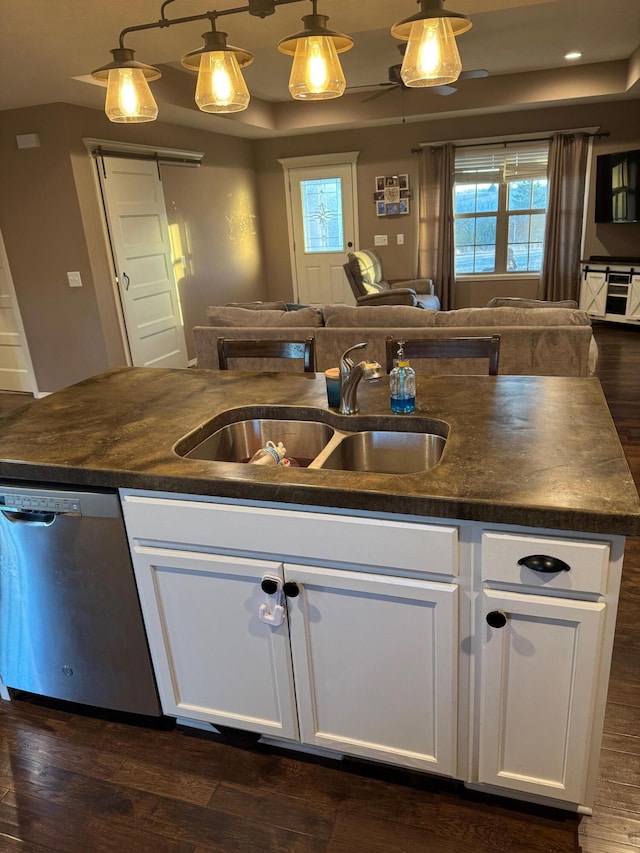 kitchen with a sink, dark countertops, open floor plan, and dishwasher