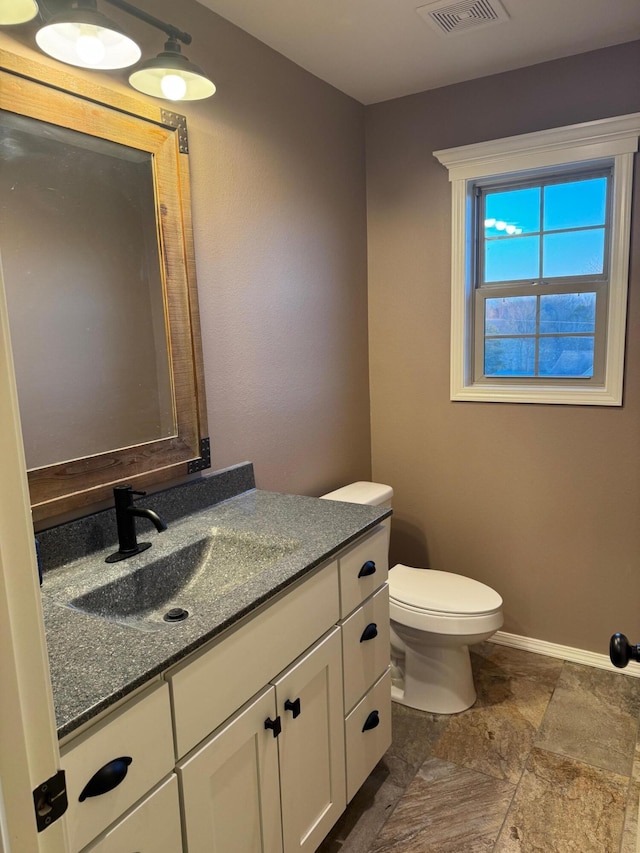 half bath featuring toilet, baseboards, visible vents, and vanity