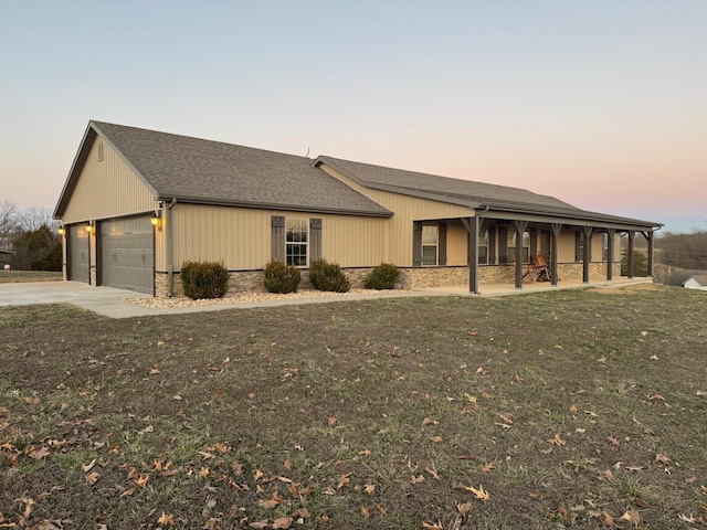 view of front facade with stone siding, a shingled roof, a lawn, and concrete driveway