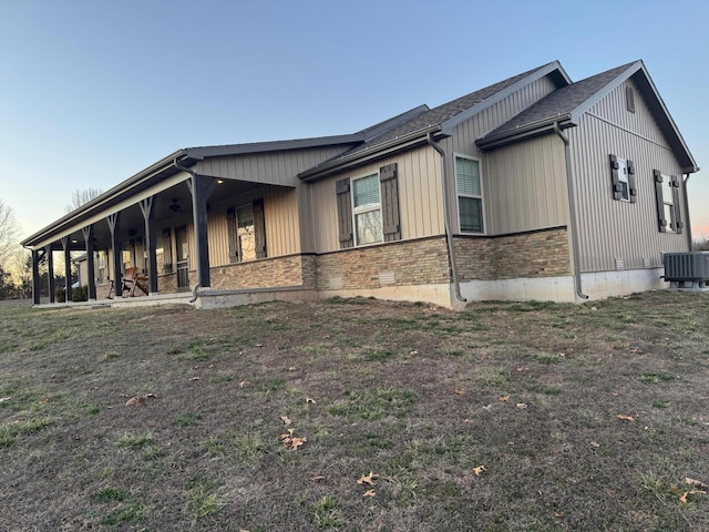 view of property exterior with stone siding, central AC unit, and a lawn