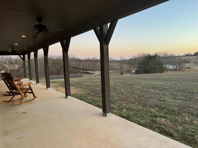 patio terrace at dusk featuring ceiling fan and a yard