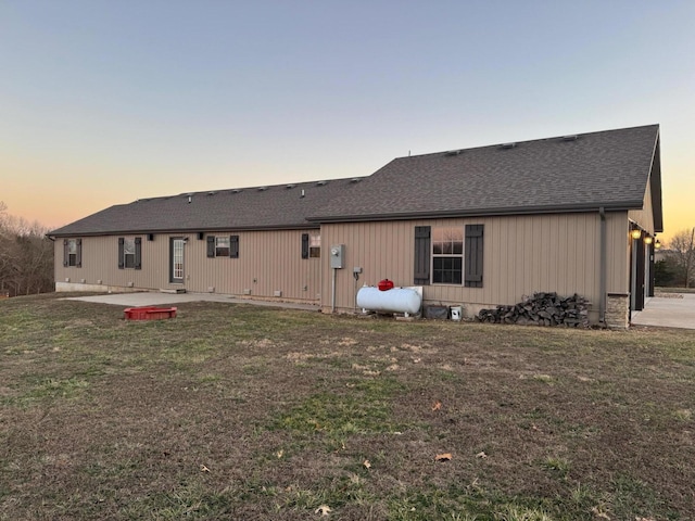 back of property at dusk featuring a patio area, roof with shingles, and a yard