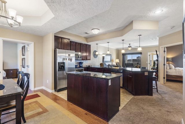 kitchen with a center island, dark countertops, appliances with stainless steel finishes, dark brown cabinets, and a peninsula