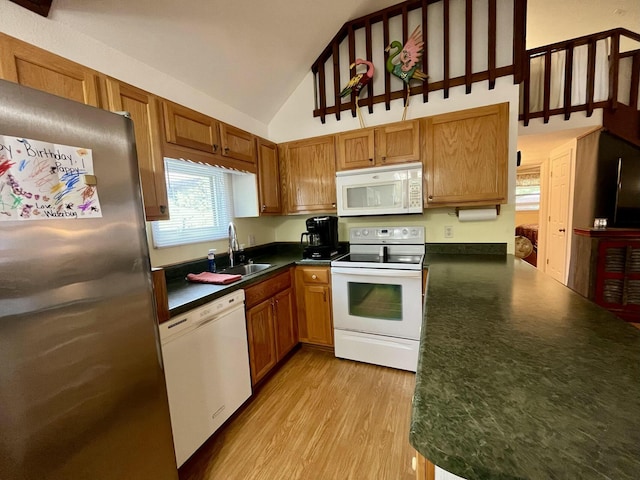 kitchen featuring white appliances, a sink, light wood-type flooring, brown cabinetry, and dark countertops