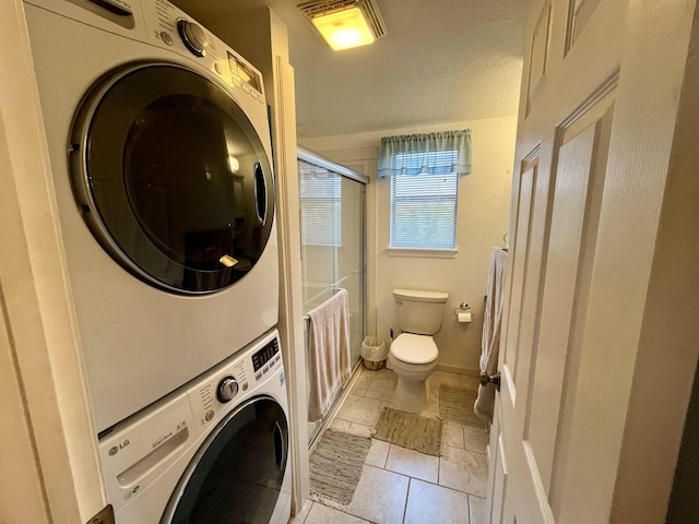 washroom with visible vents, a textured ceiling, stacked washing maching and dryer, laundry area, and baseboards