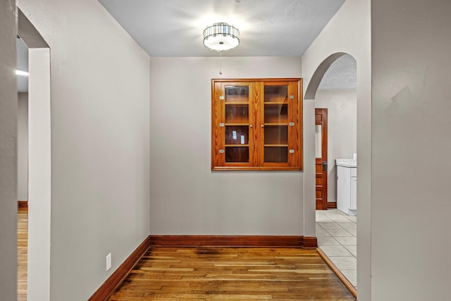 corridor with arched walkways, baseboards, and wood finished floors