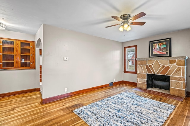 living area featuring hardwood / wood-style flooring, a fireplace, baseboards, and arched walkways